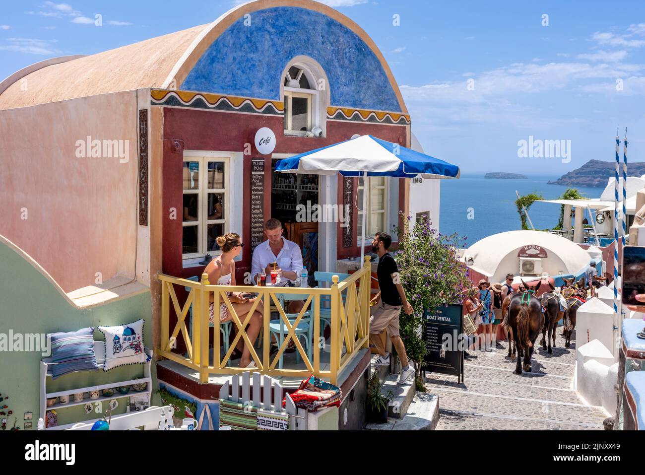 Una pareja se sienta con bebidas en la pequeña terraza de Un café en la ciudad de Oia, Santorini, las islas griegas, Grecia. Foto de stock