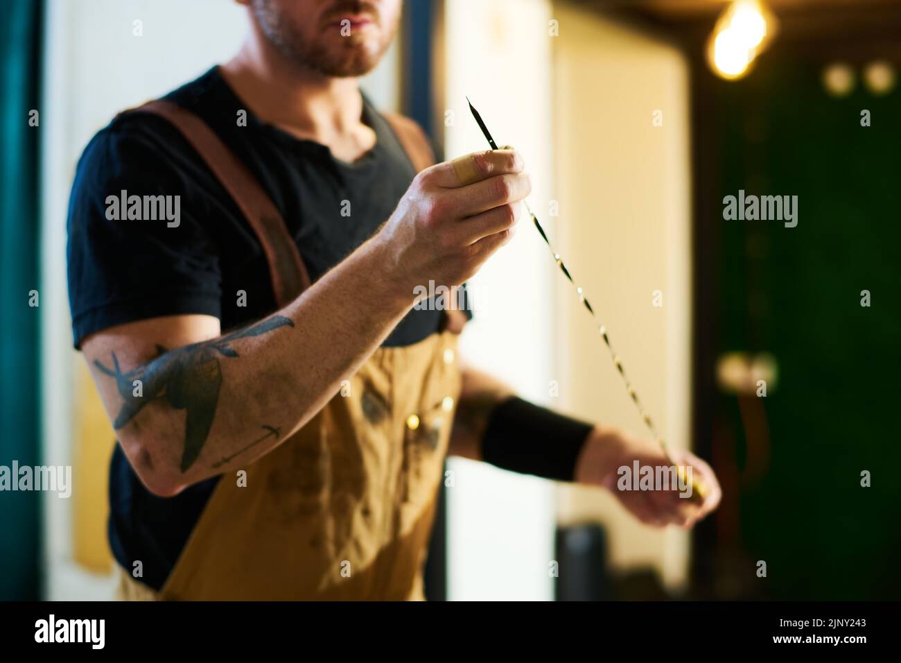 Técnico joven en el delantal que sostiene un alambre metálico afilado mientras prepara el instrumento de trabajo para comprobar el motor de un vehículo roto Foto de stock