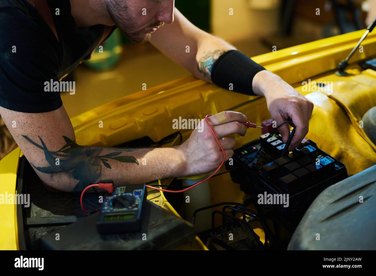 Manos de un joven técnico que se inclina sobre el motor del coche y utiliza un multímetro mientras comprueba el nuevo equipo después de la reparación Foto de stock