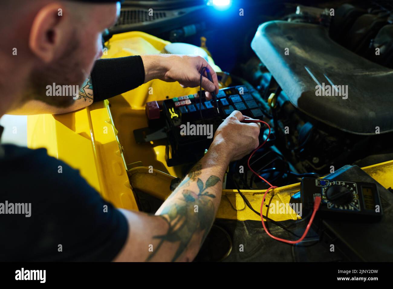 Mecánico de servicio de mantenimiento realizando diagnósticos técnicos de motor de coche y otras piezas con ayuda de multímetro digital Foto de stock