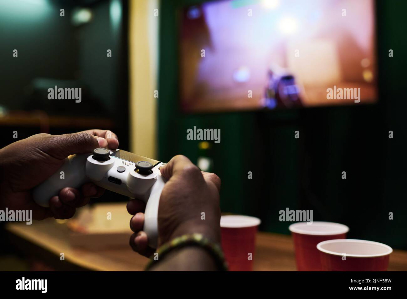 Manos del joven afroamericano pulsando los botones del mando mientras dirige el dispositivo en la pantalla del televisor durante el videojuego Foto de stock