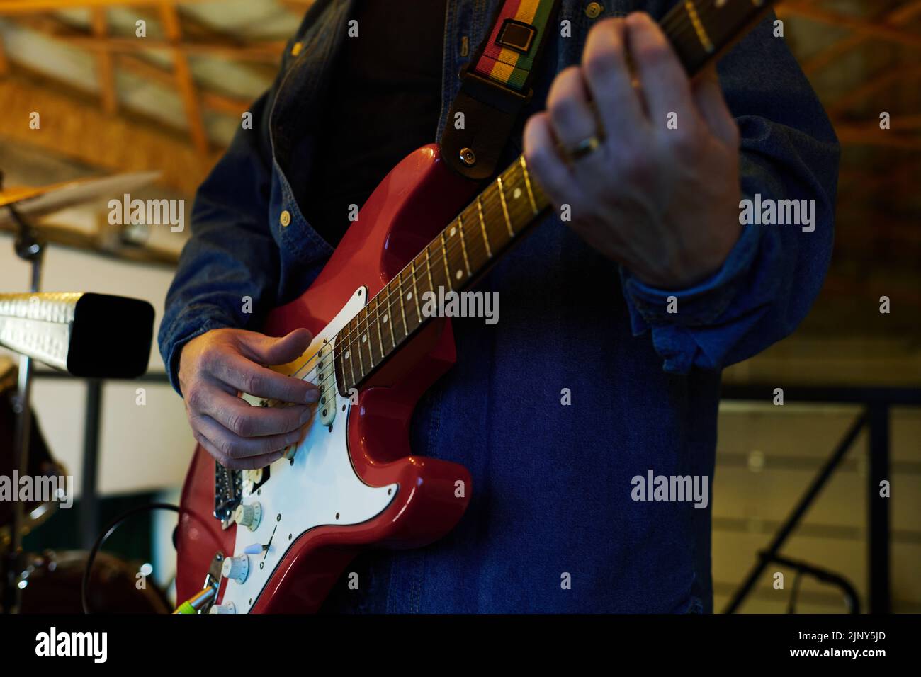 Primer plano de un joven músico en chaqueta de vaquero azul, tocando la guitarra eléctrica durante la repetición de música en el garaje Foto de stock