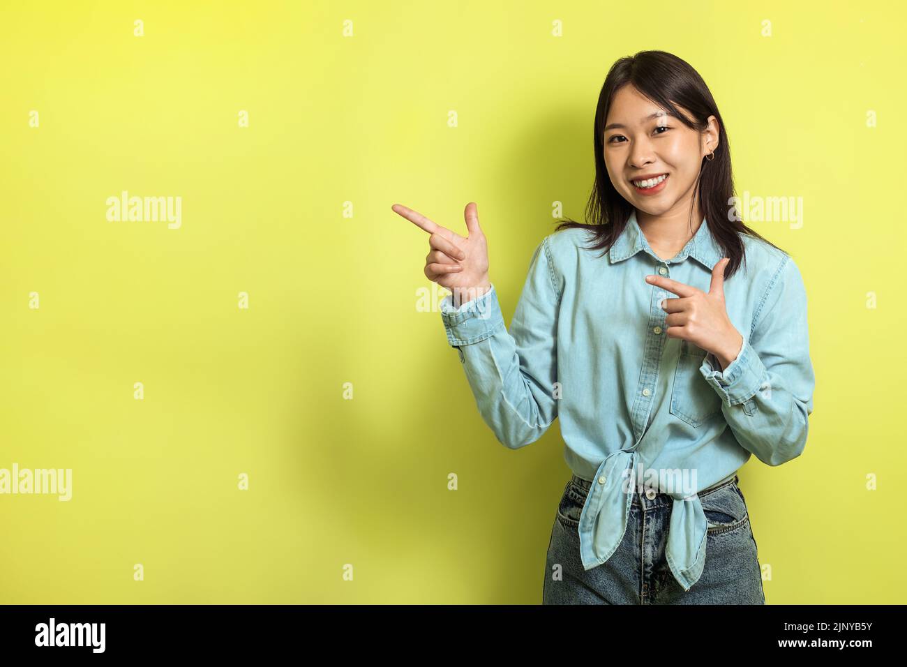 Feliz mujer china señalando los dedos a un lado en el fondo amarillo Foto de stock