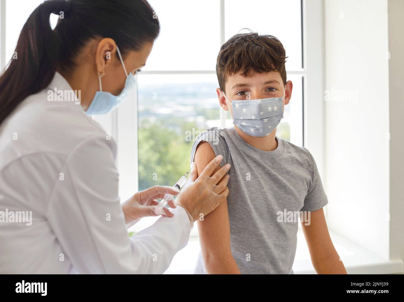 Niño escolar con mascarilla médica recibiendo una vacuna que lo protegerá durante una pandemia Foto de stock
