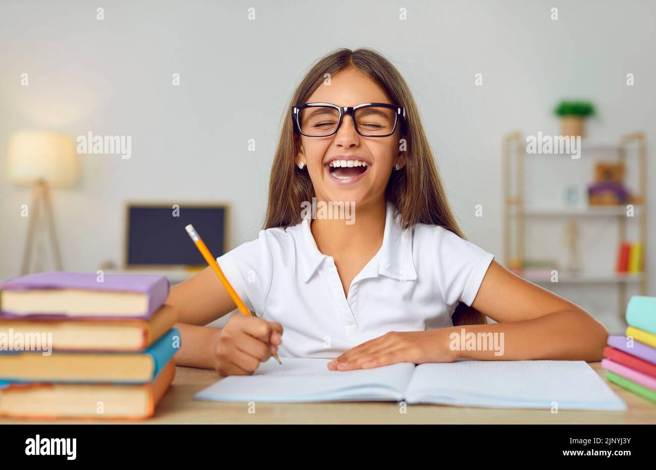 Niña estudiante feliz en gafas divertirse mientras hacía su tarea escolar Foto de stock