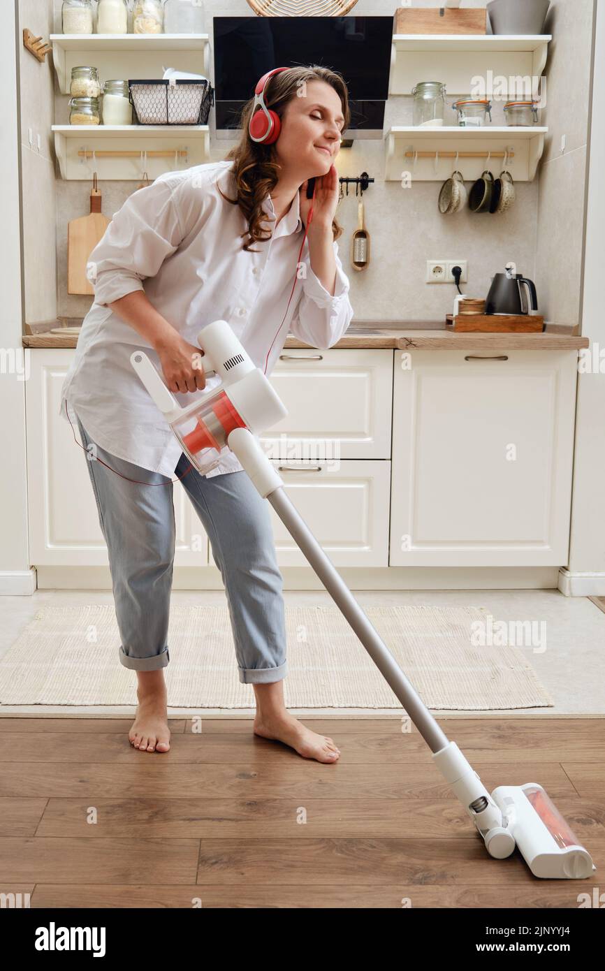 Una mujer sonriente escucha música con auriculares mientras limpia el polvo  con una aspiradora portátil inalámbrica. Una mujer feliz mientras limpiaba  el piso en una apa Fotografía de stock - Alamy