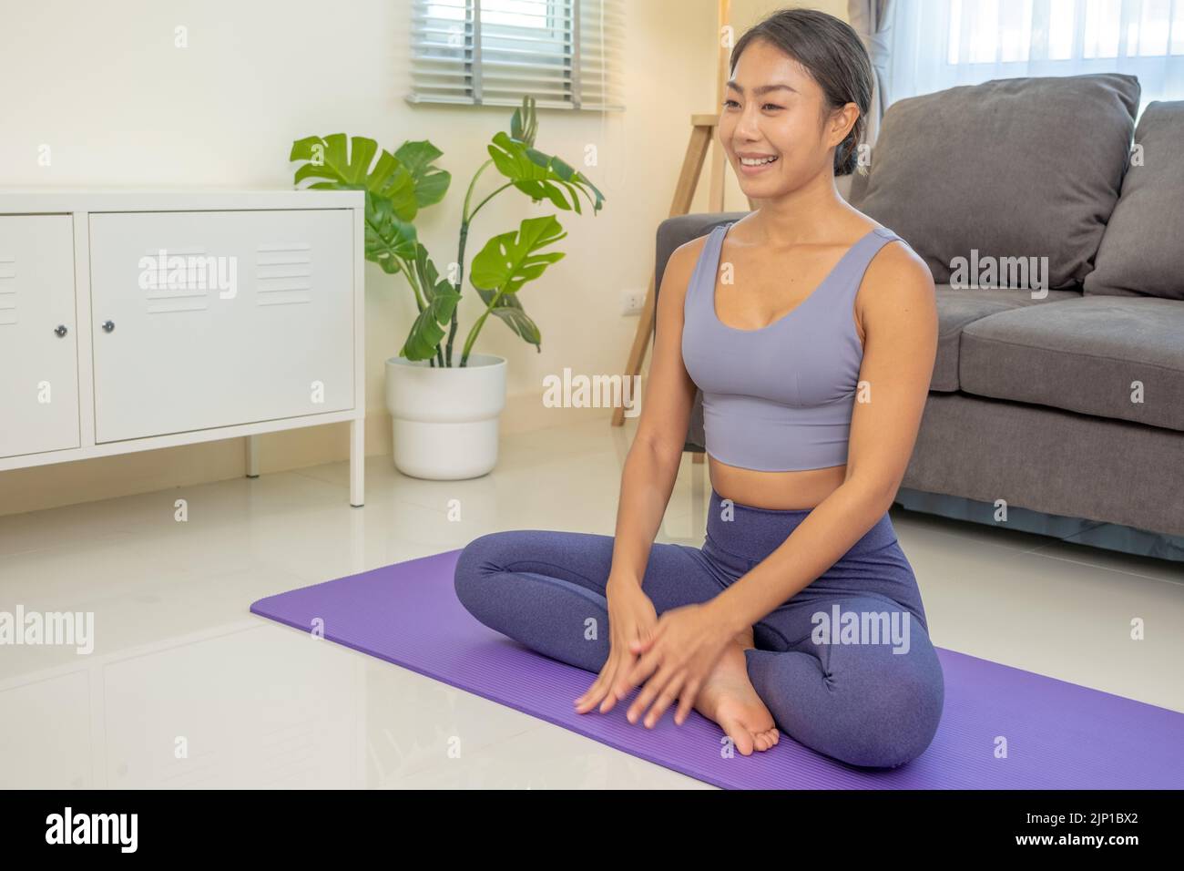 Gente asiática que practica clases de yoga sobre una colchoneta en la sala de estar. Las mujeres jóvenes con artículos deportivos enseñan a ejercitar el entrenamiento de yoga en casa Foto de stock