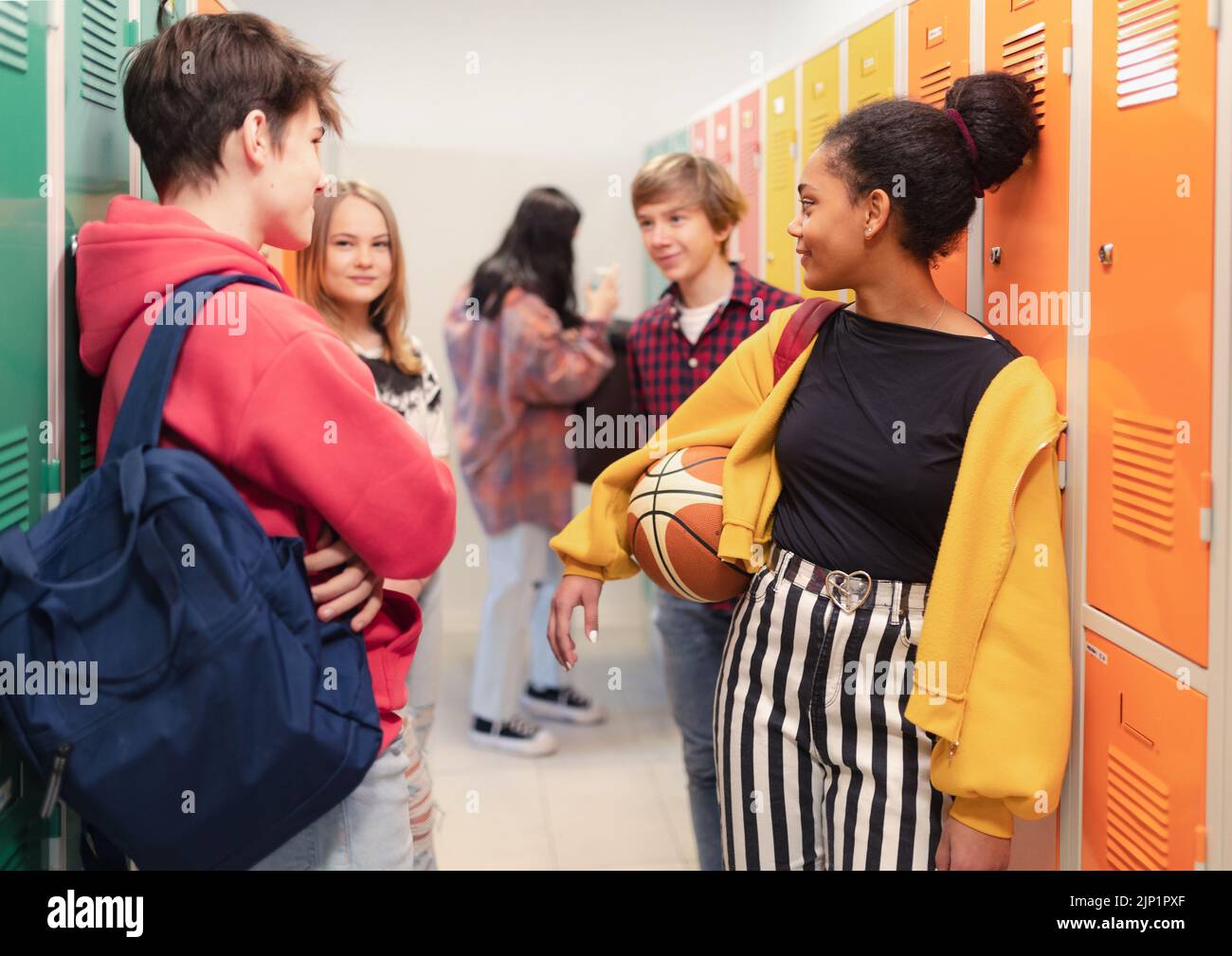 Jóvenes estudiantes de secundaria reunidos y saludando cerca del casillero en el pasillo del campus, concepto de regreso a la escuela. Foto de stock