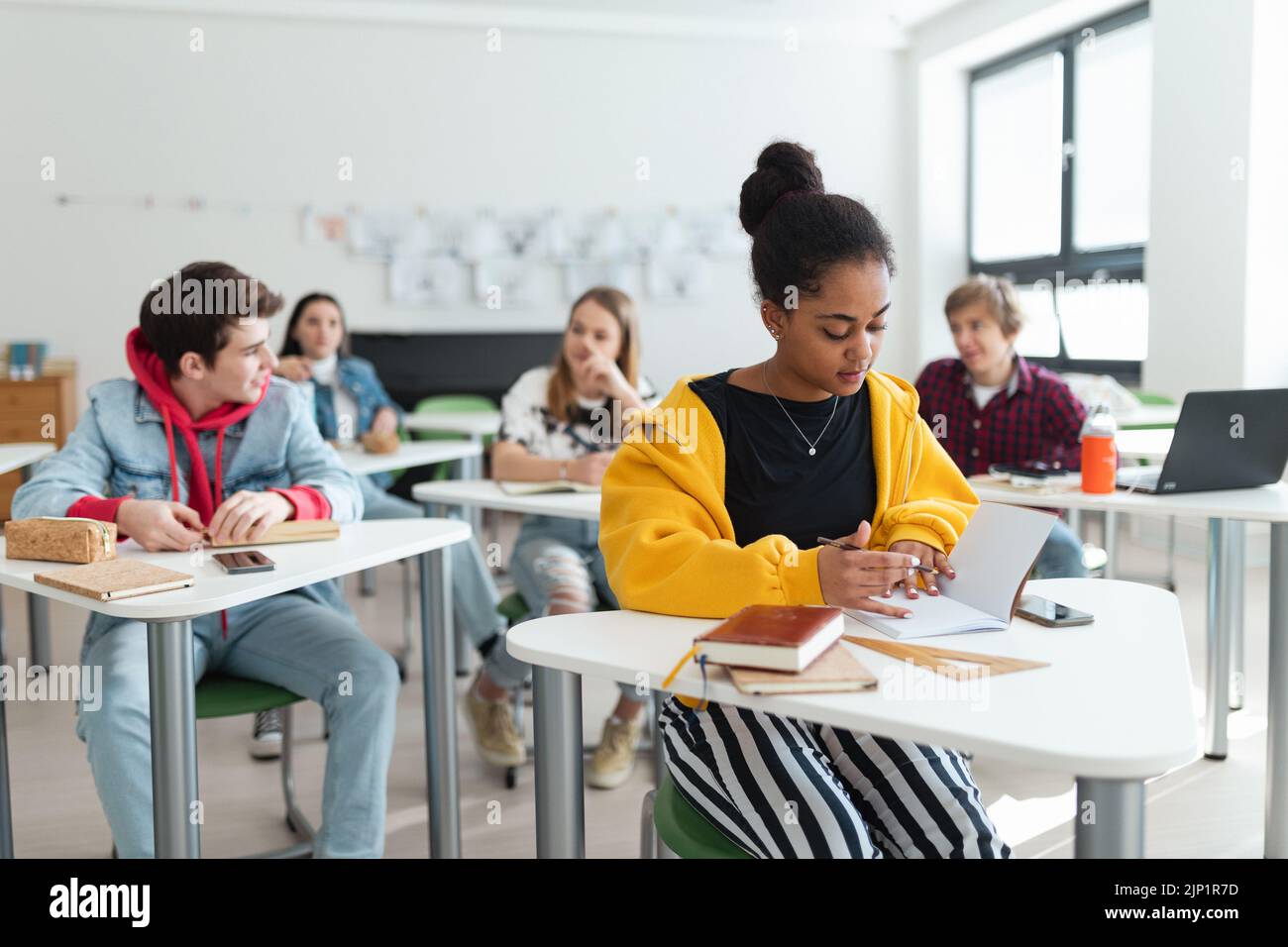 Los estudiantes de secundaria prestan atención en clase, sentados en sus escritorios y escribiendo notas, concepto de regreso a la escuela. Foto de stock