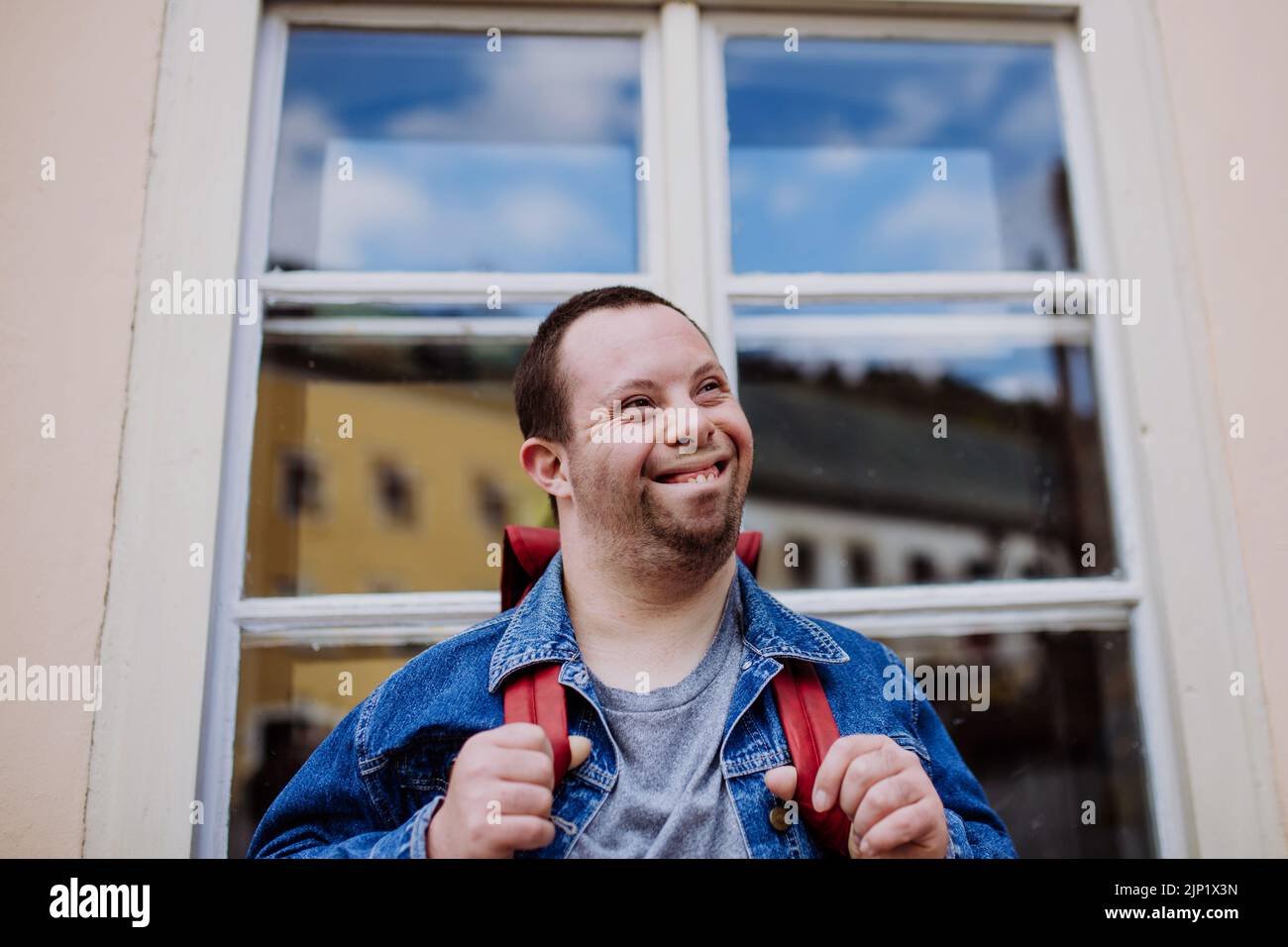 Retrato del joven feliz con sidrome de Down con mochila en la calle, sonriendo. Foto de stock