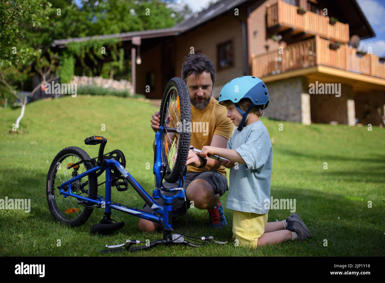 Padre con hijo pequeño juntos preparando bicicleta para un paseo, bombeando neumáticos en el jardín en frente de la casa. Foto de stock