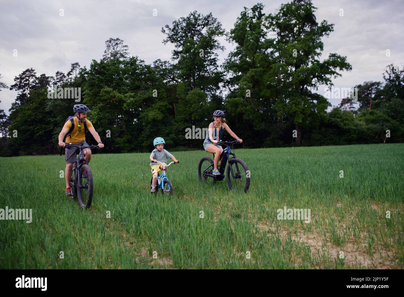Familia joven con niño pequeño montando bicicletas en el prado en el pueblo en verano. Foto de stock