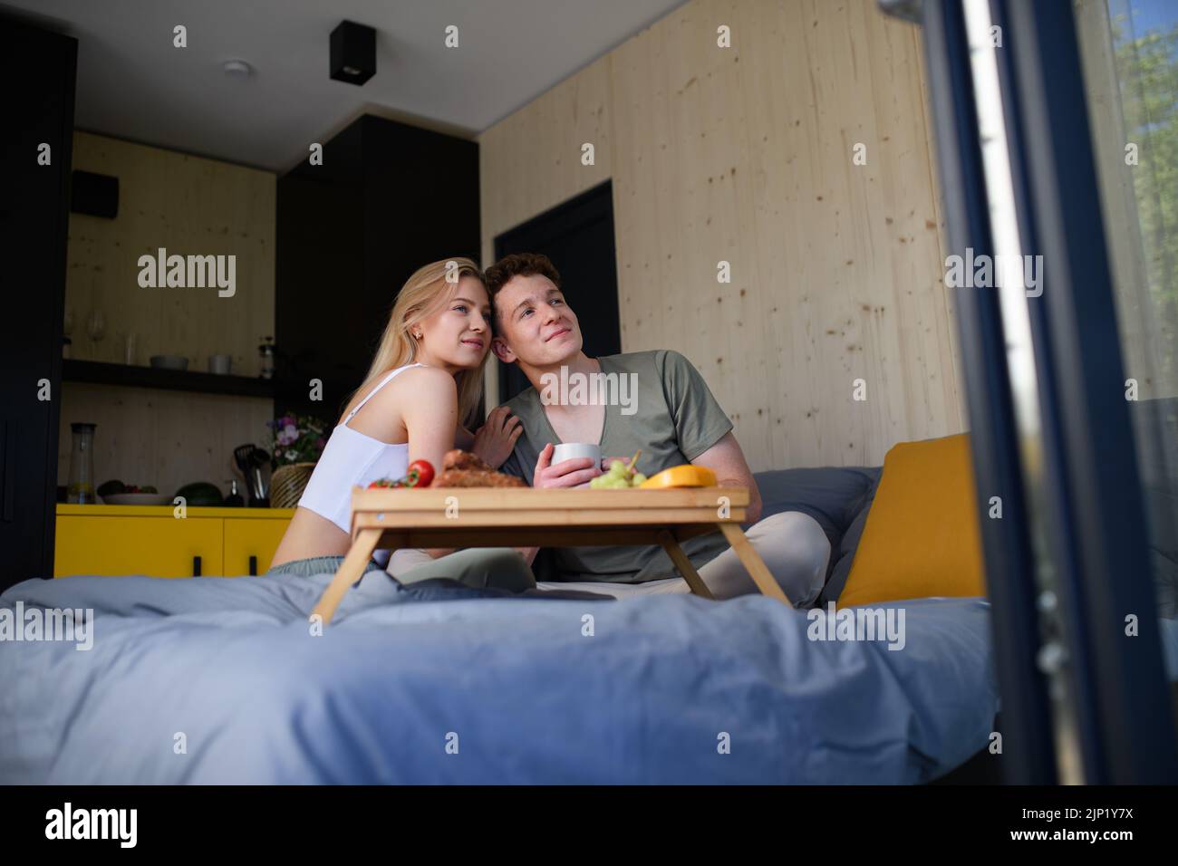 Una pareja joven y hermosa enamorada está sentada en la cama y tomando un desayuno saludable juntos. Foto de stock