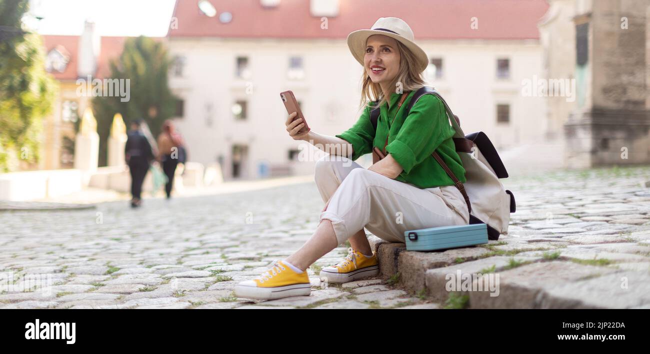 Mujer joven viaja sola por el casco antiguo de la ciudad, sentada y utilizando un smartphone. Foto de stock