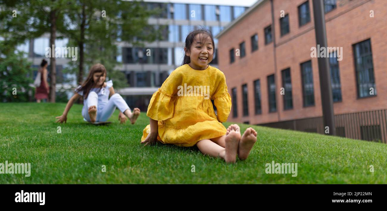 Chica asiática tratando de patinar con su amiga en el parque de la ciudad, concepto de niños activos. Fotografía amplia. Foto de stock