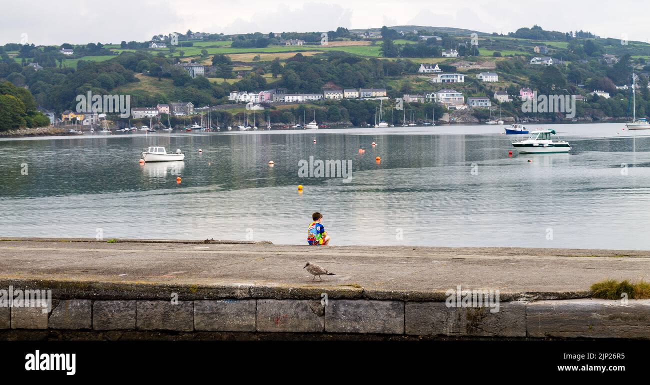 Niño pequeño sentado en soledad en la pared del puerto solo mirando al mar. Foto de stock