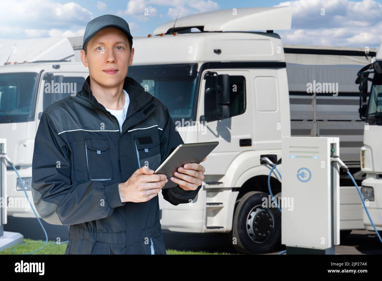 Gestor de flotas con una tableta digital junto a camiones eléctricos en estaciones de carga de vehículos eléctricos Foto de stock