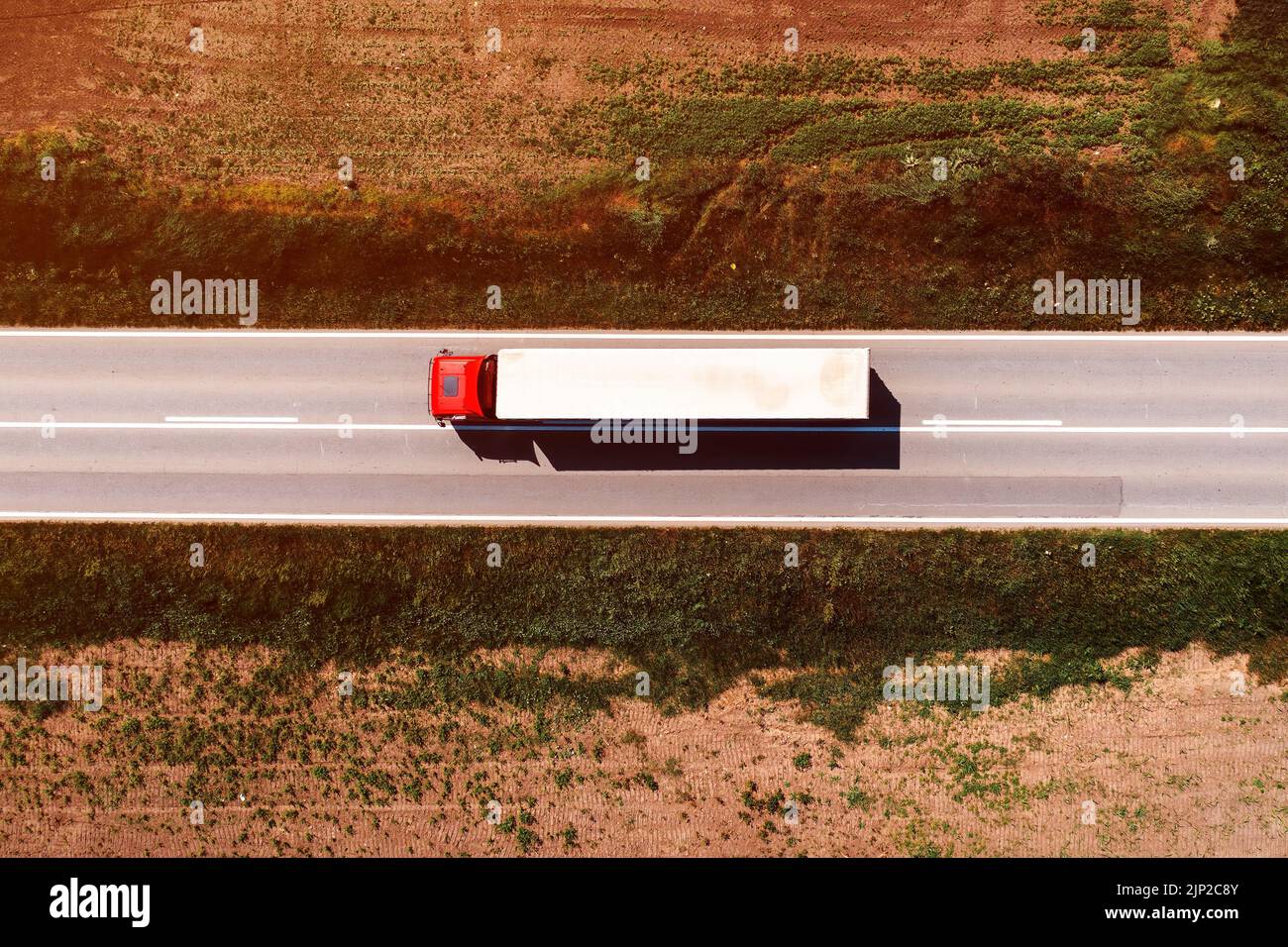 Toma aérea de un camión que conduce a lo largo de la autopista a través de paisajes rurales, con un punto de vista directo sobre el soleado día de la primavera. Transporte y lo Foto de stock