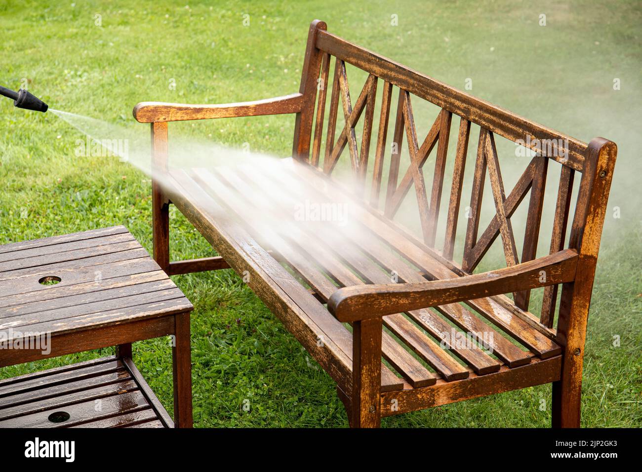 Vista de cerca de la persona que trabaja limpieza a presión lavar muebles de madera de jardín banco al aire libre en verano. Foto de stock