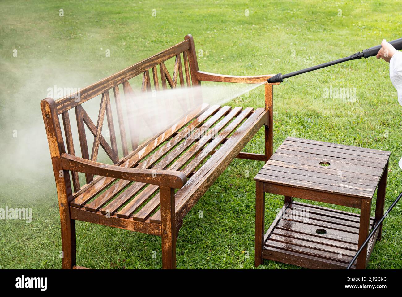 Vista de cerca de la persona que trabaja limpieza a presión lavar muebles de madera de jardín banco al aire libre en verano. Foto de stock