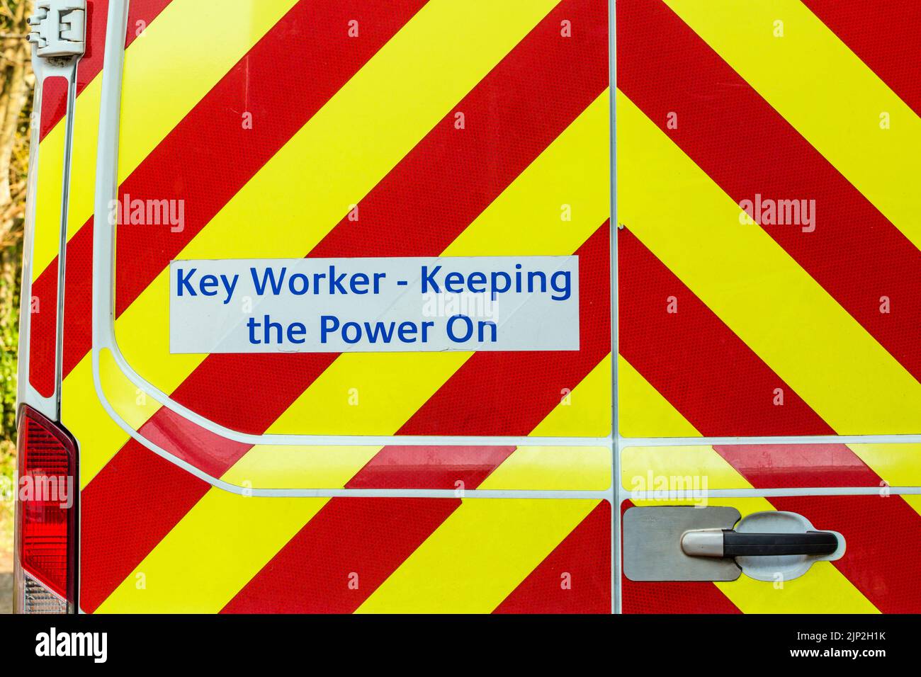 Trabajador clave que mantiene el cartel de encendido en la parte trasera de una furgoneta de una compañía eléctrica, Reino Unido Foto de stock
