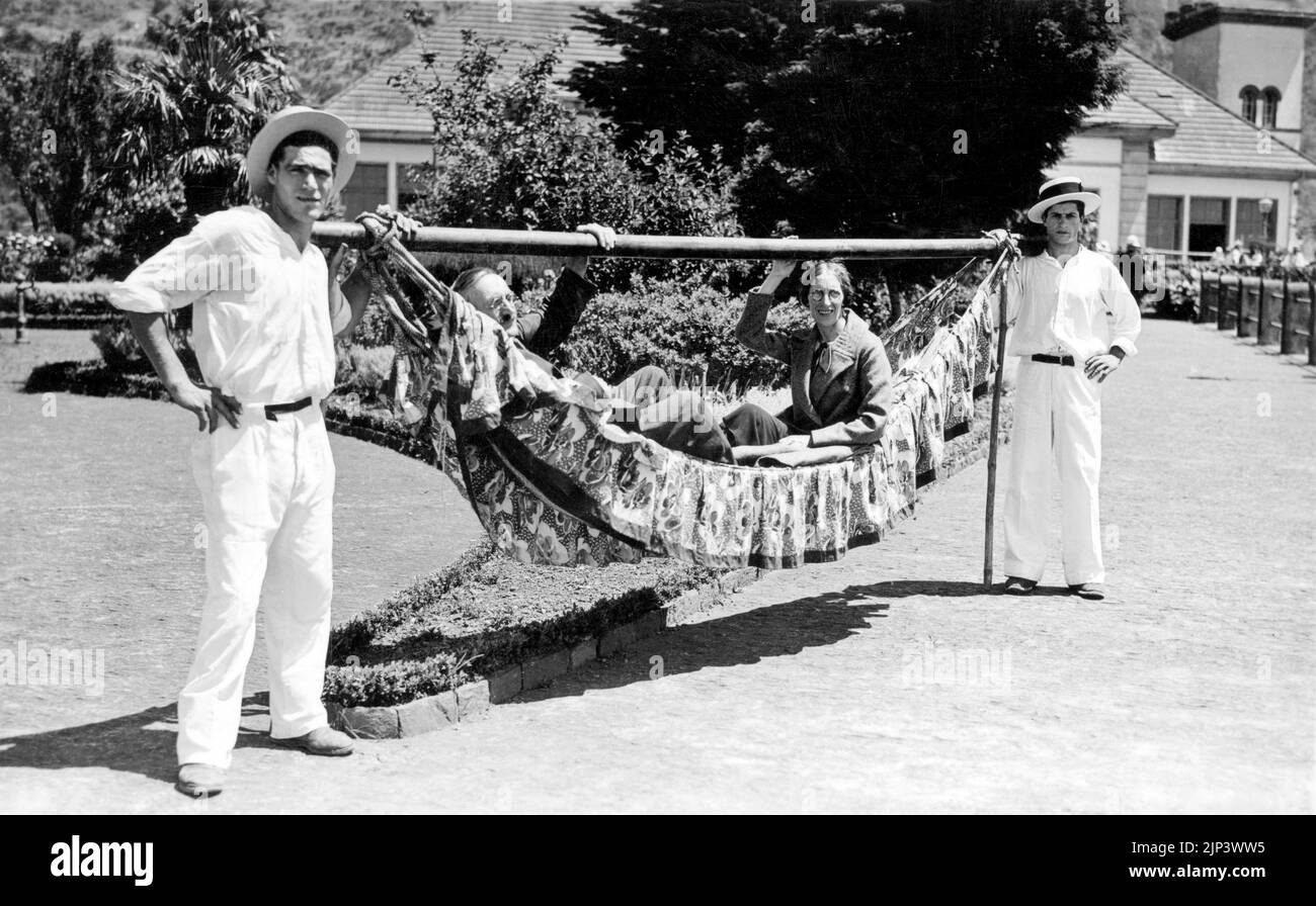 'Otro método de viaje' fotografía vintage de una hamaca de mano llevada por 2 hombres con una pareja sentada en el interior. Foto de stock