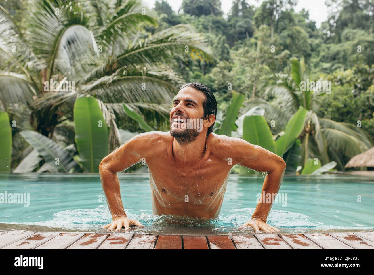 Retrato de un joven guapo en la piscina. Hombre caucásico en la piscina mirando lejos y sonriendo. Hombre en un complejo de vacaciones de lujo. Foto de stock