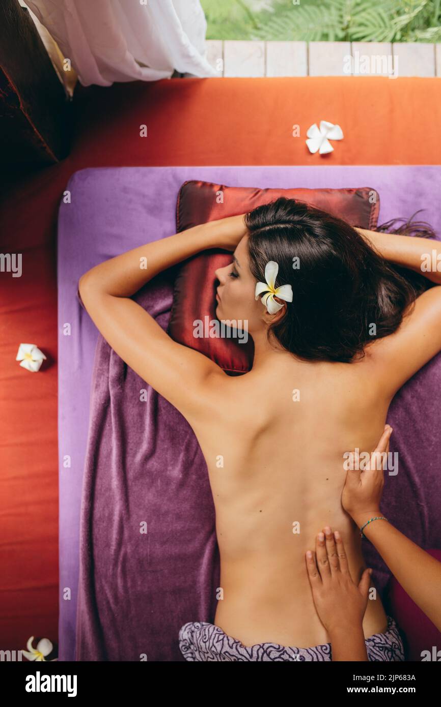 Vista superior de la atractiva joven mujer caucásica tumbada en una mesa de masaje recibiendo un masaje de espalda en el spa de día. Mujer recibiendo masaje de cuerpo entero. Foto de stock