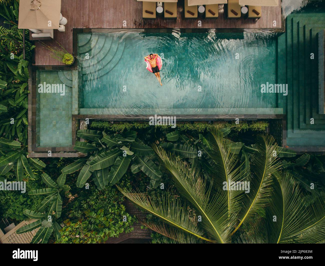 Foto aérea del joven descansando en la piscina del complejo. Hombre en el anillo inflable de la piscina. Foto de stock