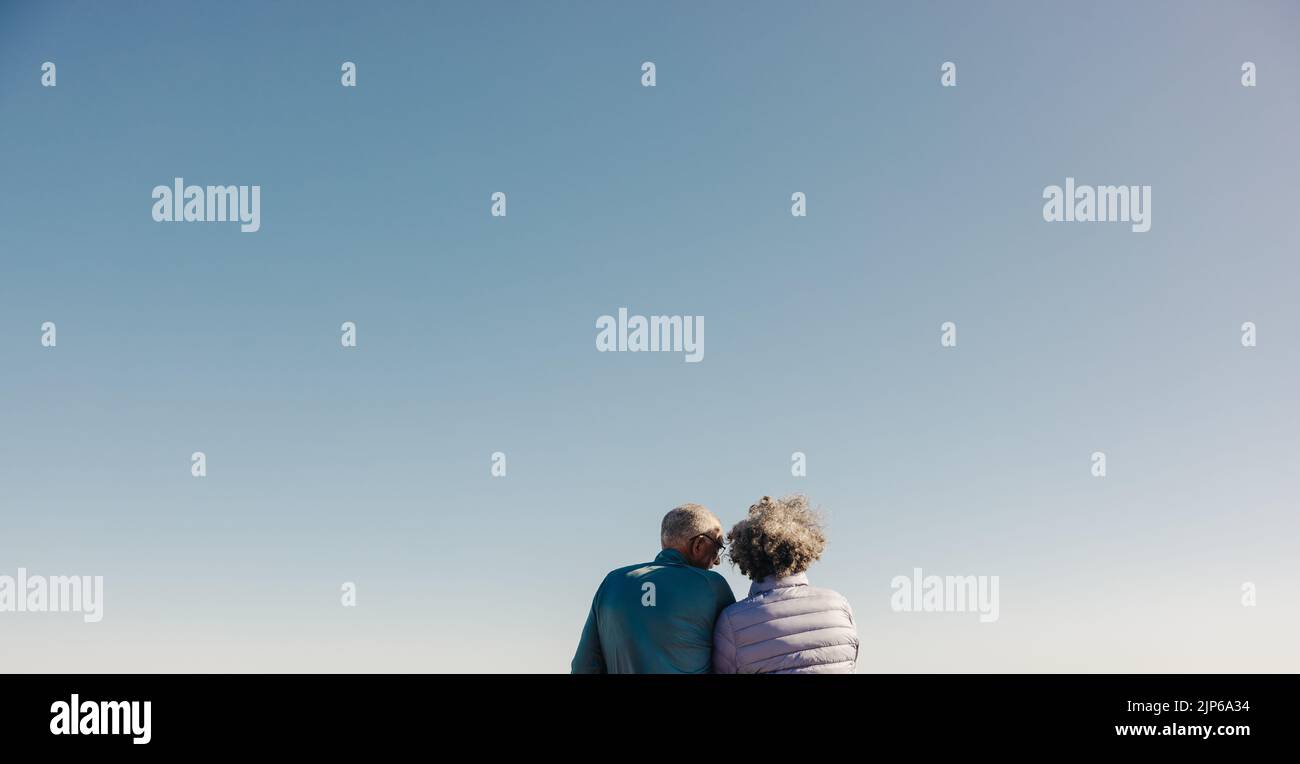 Vista trasera de una pareja mayor conversando mientras disfrutaba de una refrescante vista del cielo en la playa. Romántica pareja de ancianos disfrutando de una relajante playa Foto de stock
