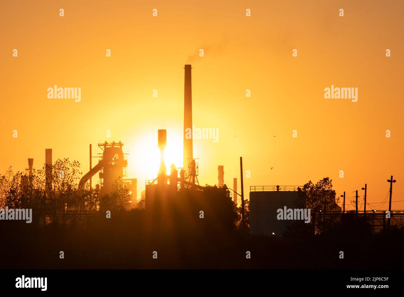 El sol de la tarde brilla una chimenea industrial, una gran fábrica al anochecer. Foto de stock