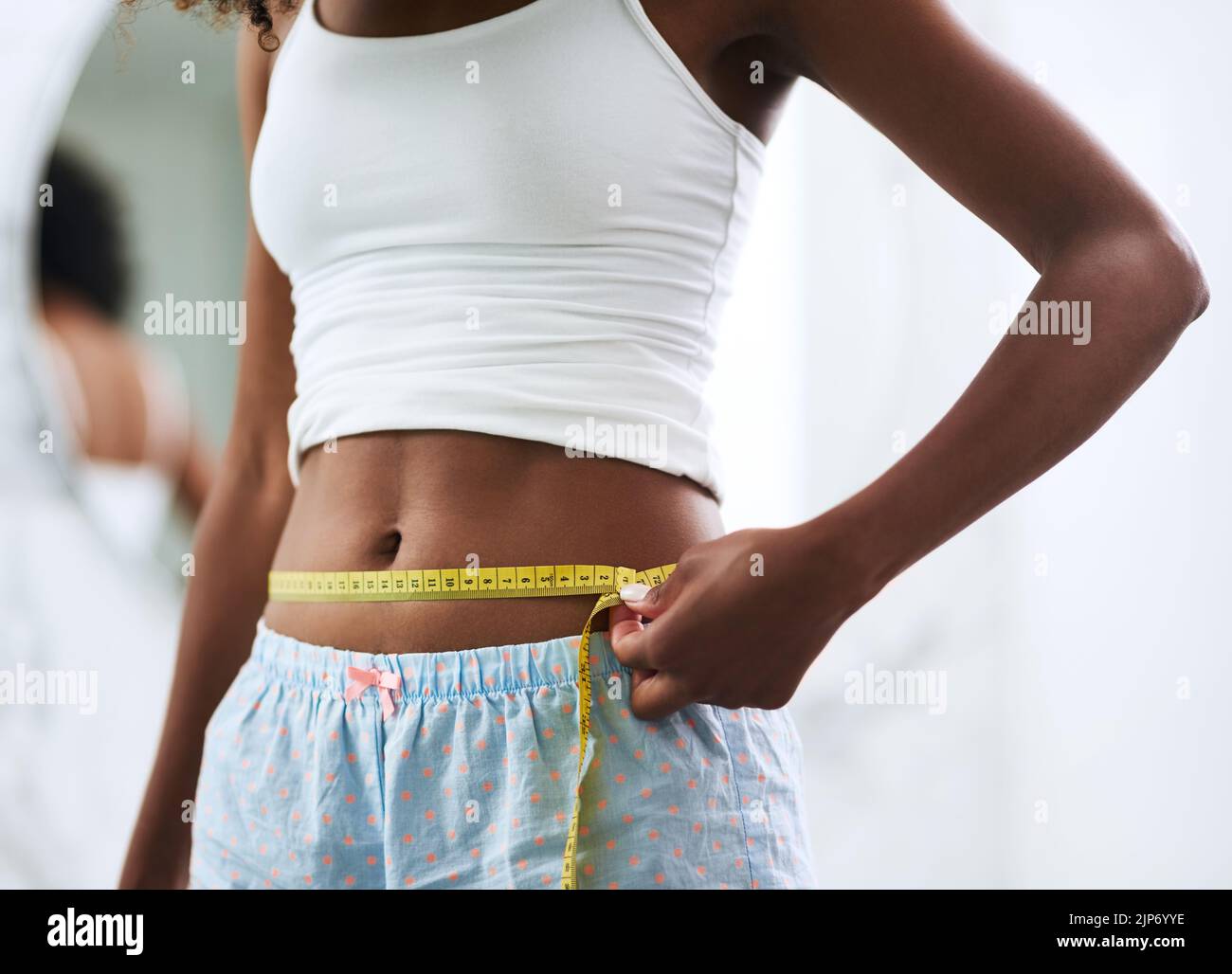 Desprendiendo las pulgadas. Primer plano de una mujer irreconocible midiendo su cintura. Foto de stock