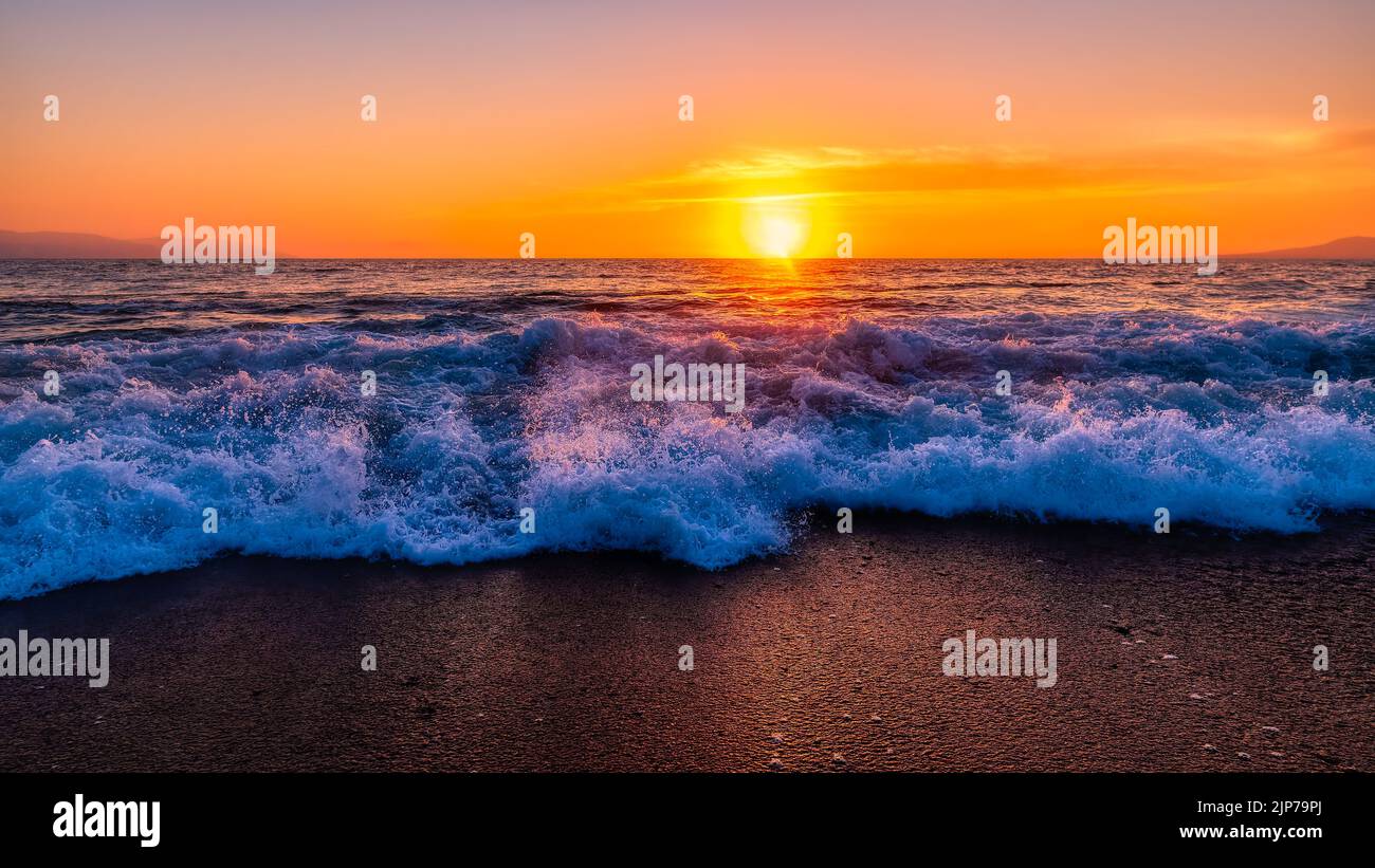 Una Ola Oceánica iluminada por la Puesta de Sol se está rompiendo en la orilla de la playa en formato de imagen de banner de alta resolución Foto de stock