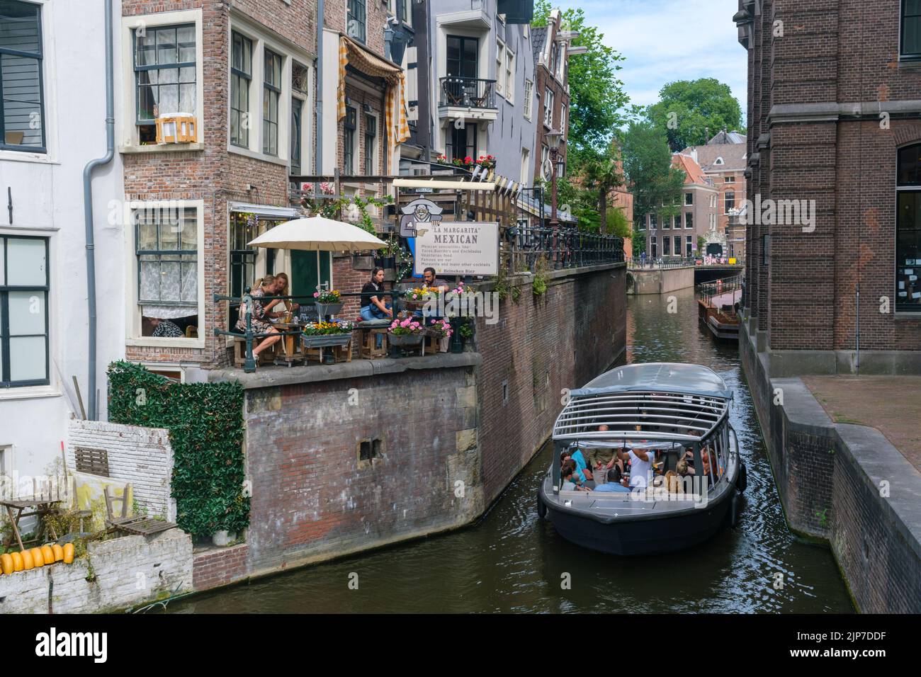 Ámsterdam, Países Bajos - 21 de junio de 2022: Barco turístico en el canal de Grimburgwal. Vista desde el puente Grimnessesluis Foto de stock