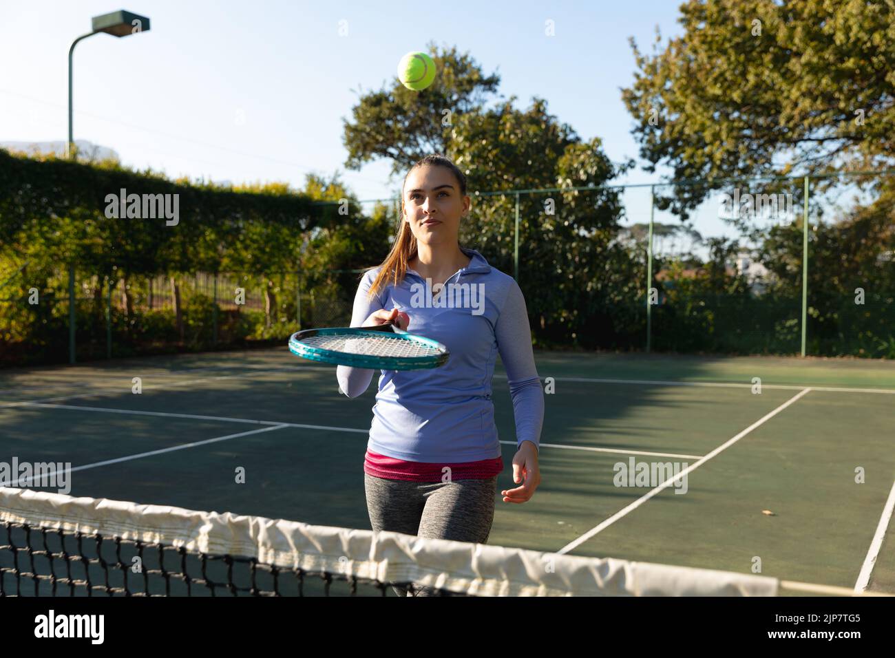 Mujer caucásica jugando tenis rebotando pelota sobre raqueta en cancha de tenis al aire libre Foto de stock