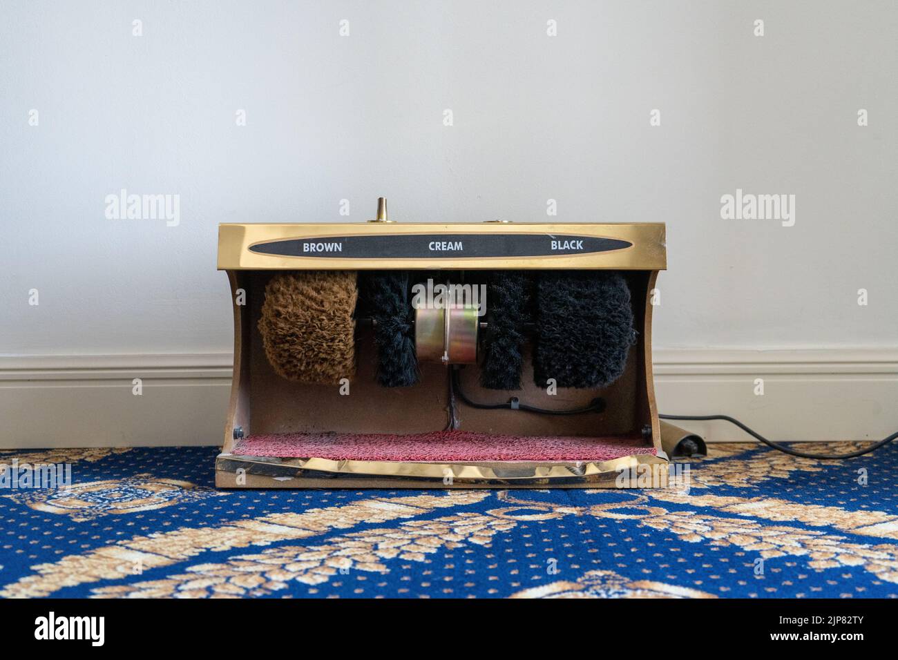 La máquina pulidora de zapatos en la alfombra azul junto a la pared Foto de stock