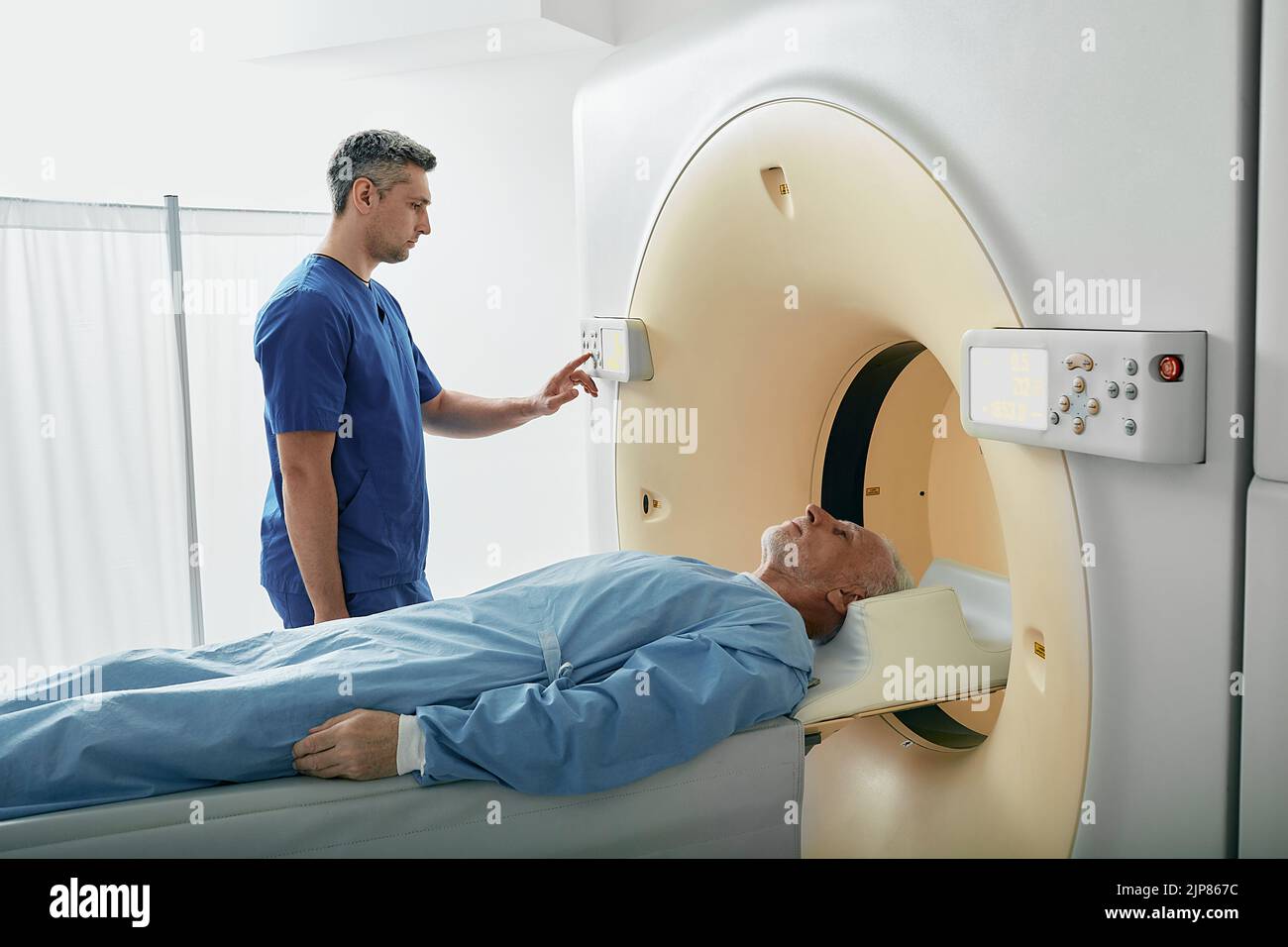 El radiógrafo que opera el escáner de tomografía computarizada que se utiliza para explorar a un paciente acostado en el departamento de radiología del hospital. Escáner de TC Foto de stock