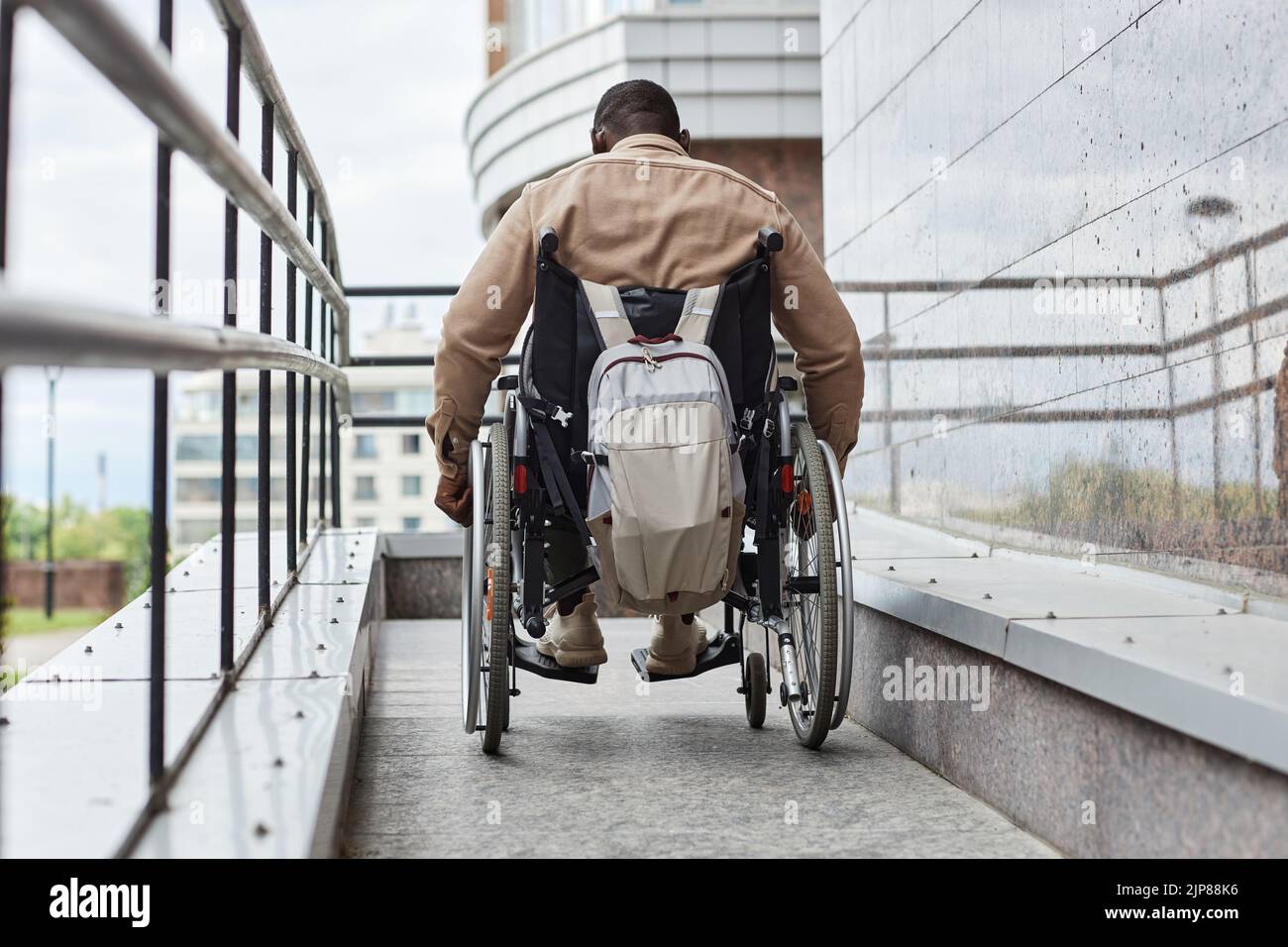 Vista posterior de un hombre con discapacidad empujando la rueda de la silla de ruedas mientras desciende por rampa en la ciudad, espacio para copias Foto de stock