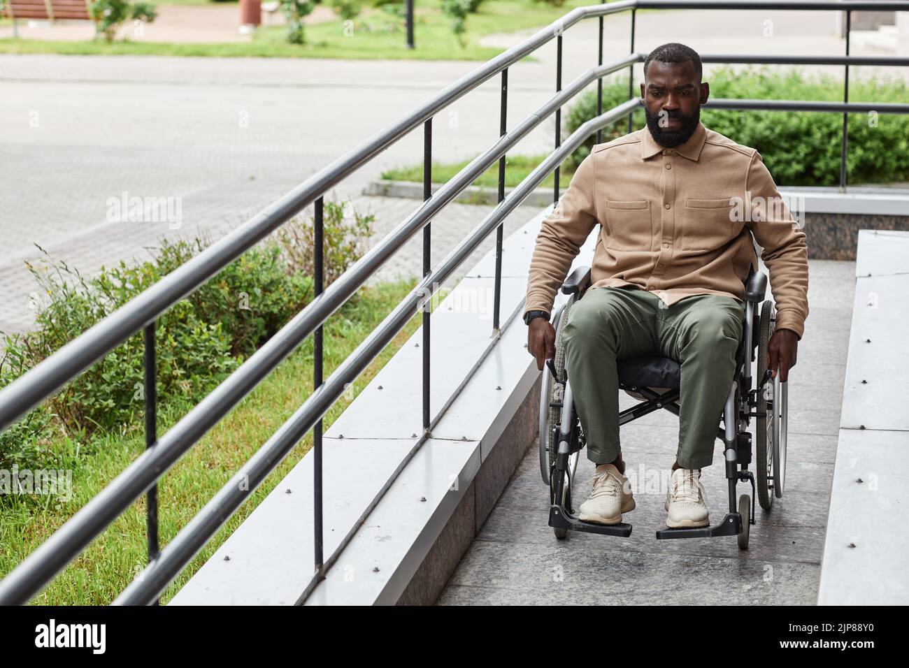 Retrato completo de hombre negro adulto con discapacidad bajando rampa en ciudad, accesibilidad urbana Foto de stock