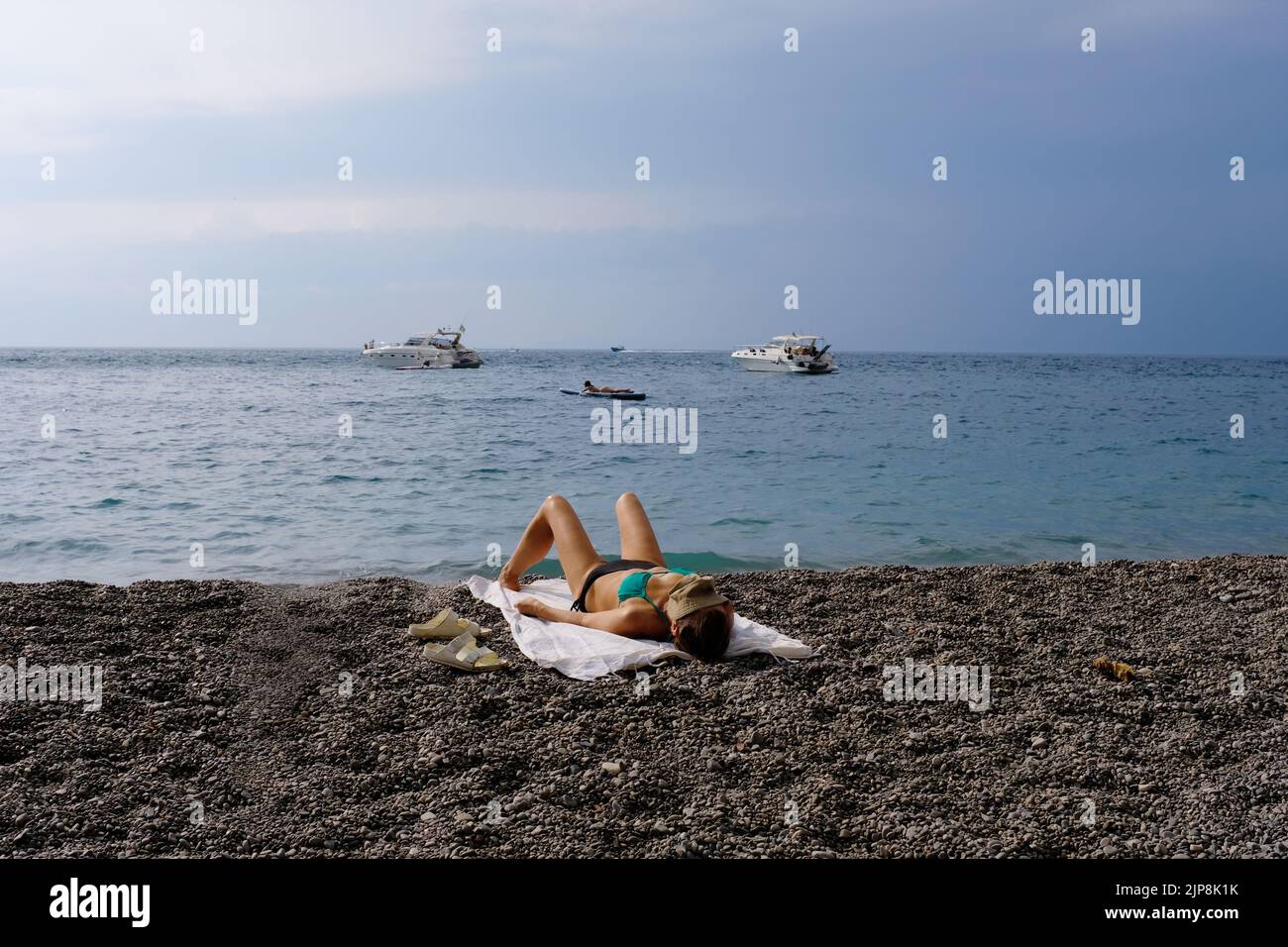Una mujer tomando el sol en una playa pública en vico equense italia con barcos en el fondo. Foto de stock