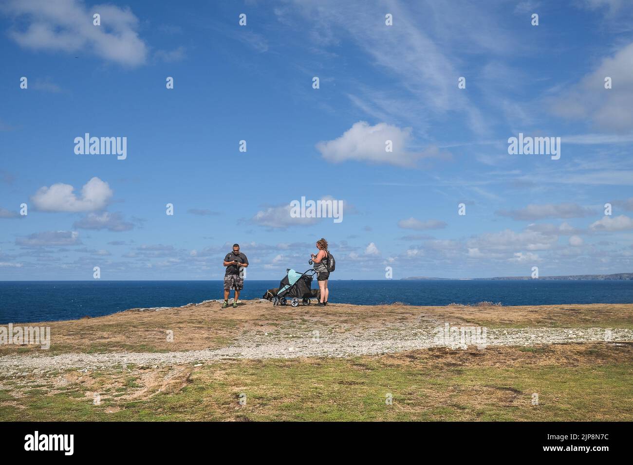 Dos veraneantes, sus perros y un cochecito mirando sus teléfonos móviles en Warren en Pentire Point East en la costa de Newquay en Cornwall. Foto de stock
