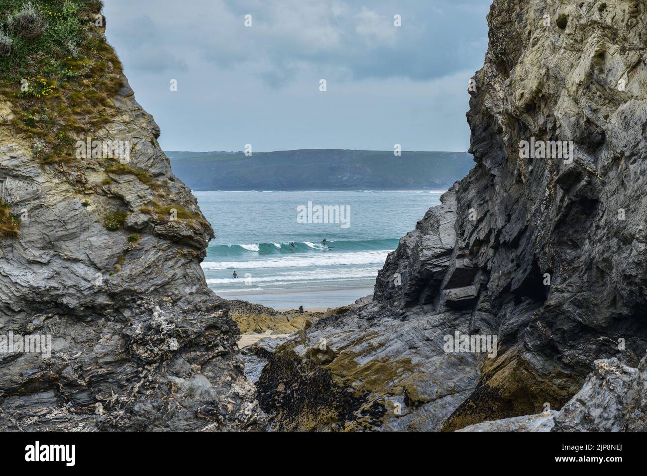 Una vista distante a través de un hueco en los acantilados de los surfistas en el mar en la playa Great Western en Newquay en Cornwall en el Reino Unido. Foto de stock