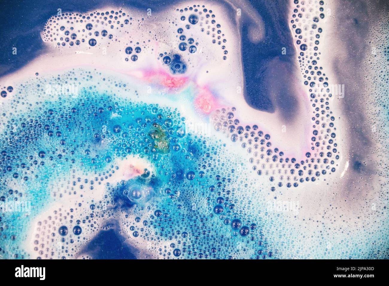 Espuma rosa y púrpura de colores en el agua azul. Espuma de baño y spa y cosméticos Foto de stock