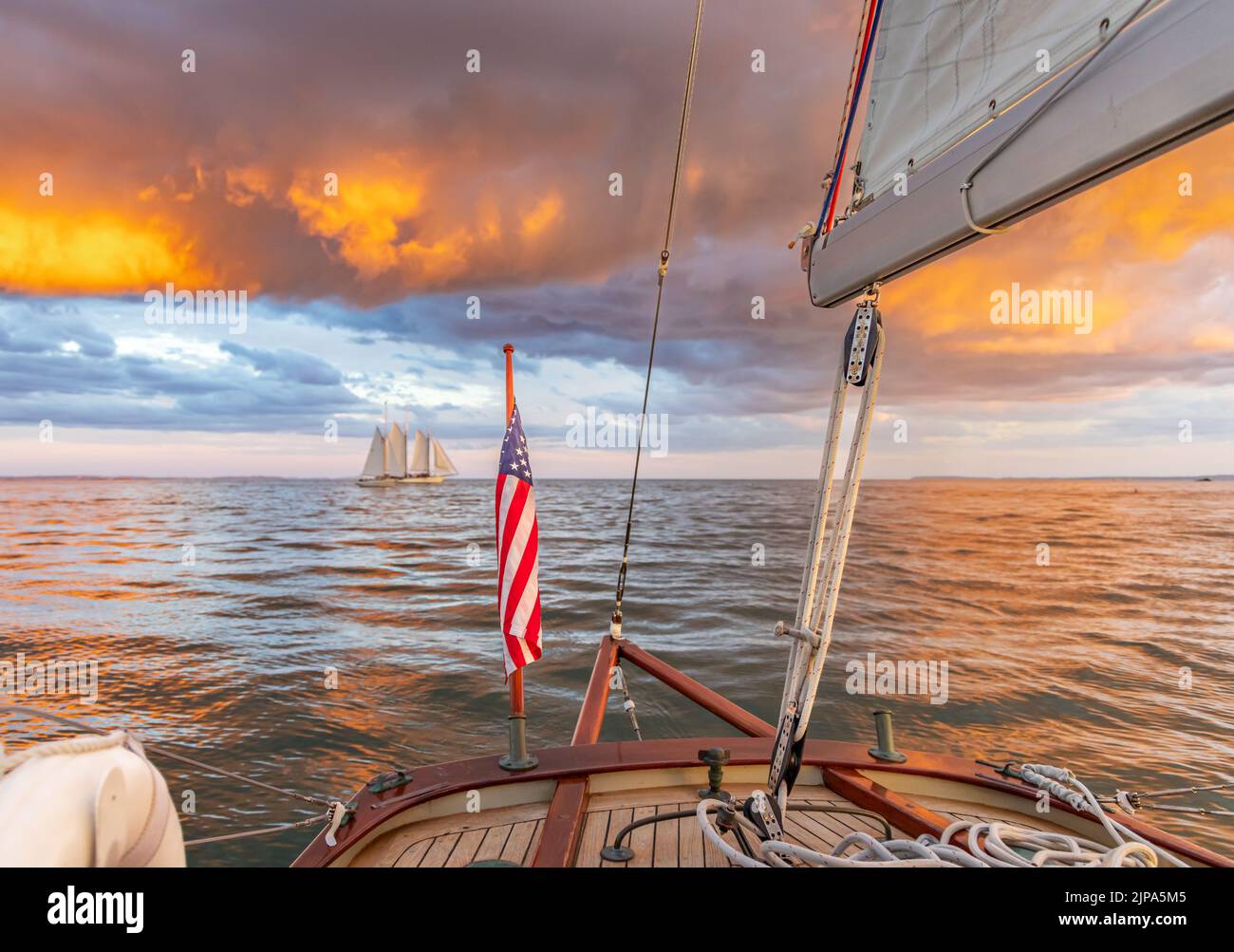 Navegación en un pequeño velero con vista a una increíble puesta de sol y velero distante Foto de stock