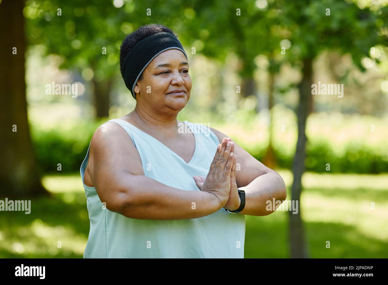 Retrato de la cintura para arriba de mujer negra madura haciendo yoga al aire libre en parque verde y mirando lejos con mindfulness, espacio de la copia Foto de stock