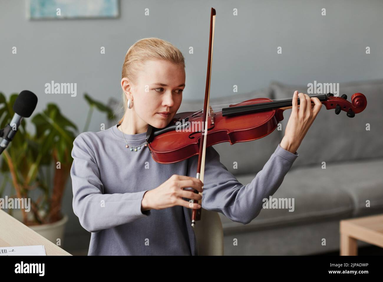 Retrato de una joven rubia tocando violín en casa o practicando en un estudio de música, espacio de copia Foto de stock