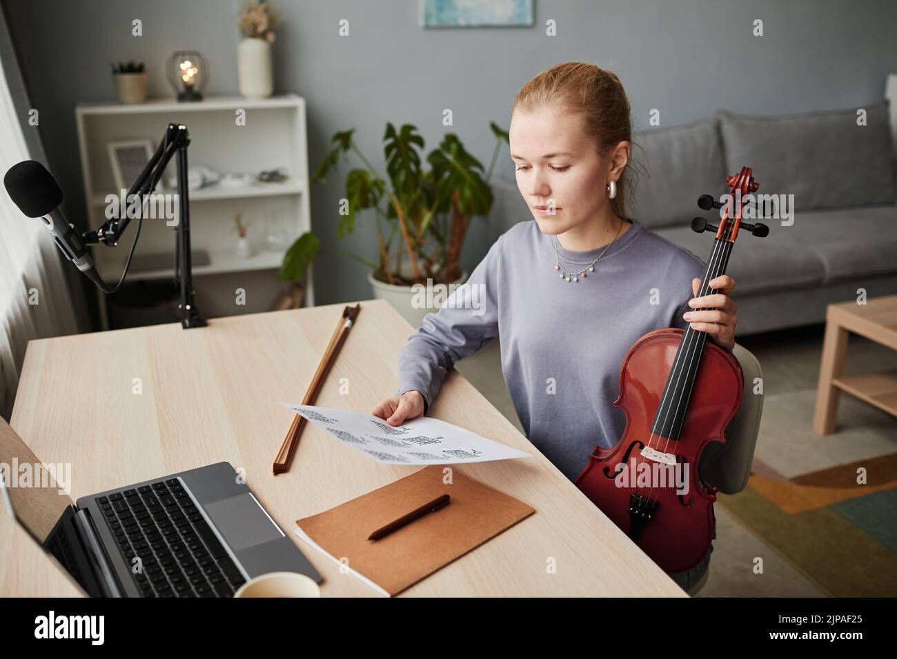 Retrato en ángulo alto de mujer rubia tocando violín en casa y mirando las hojas de música mientras componía, copiar espacio Foto de stock