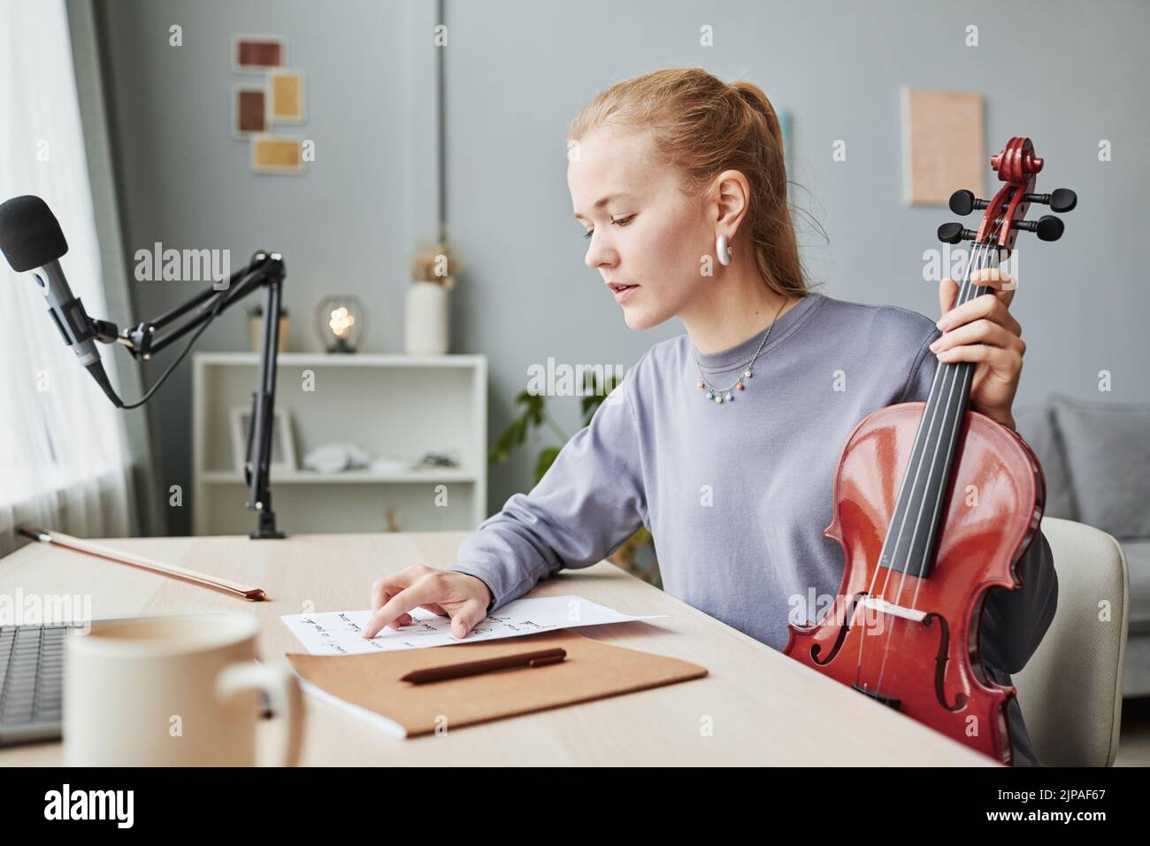 Vista lateral retrato de mujer rubia tocando violín en casa y mirando las hojas de música mientras compone, copiar espacio Foto de stock