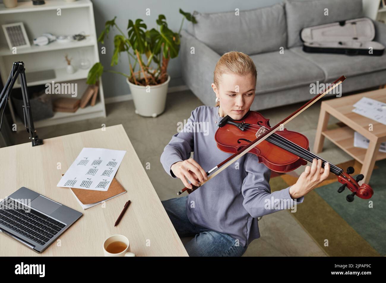 Retrato en ángulo alto de una joven rubia tocando violín en casa o practicando en un estudio de música, espacio de copia Foto de stock