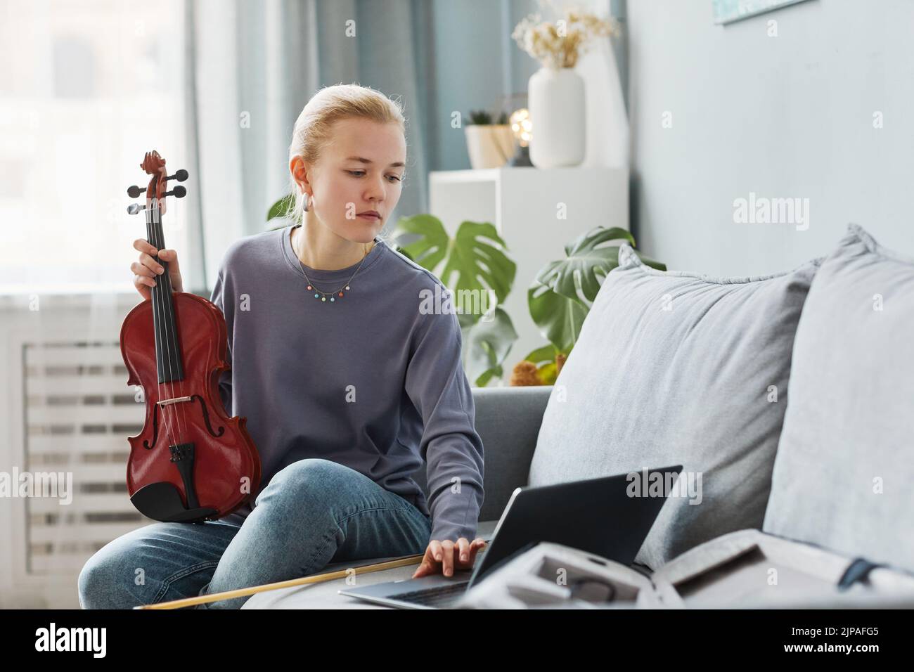 Retrato de una joven rubia tocando violín en casa y viendo una lección en línea, espacio de copia Foto de stock